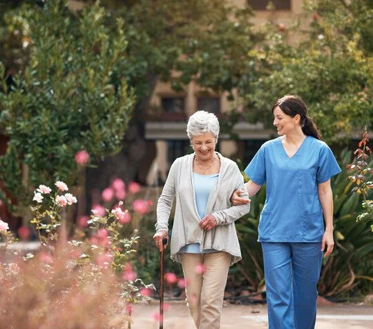 Senior woman walking with a caregiver outdoors in a senior living community on a sunny day