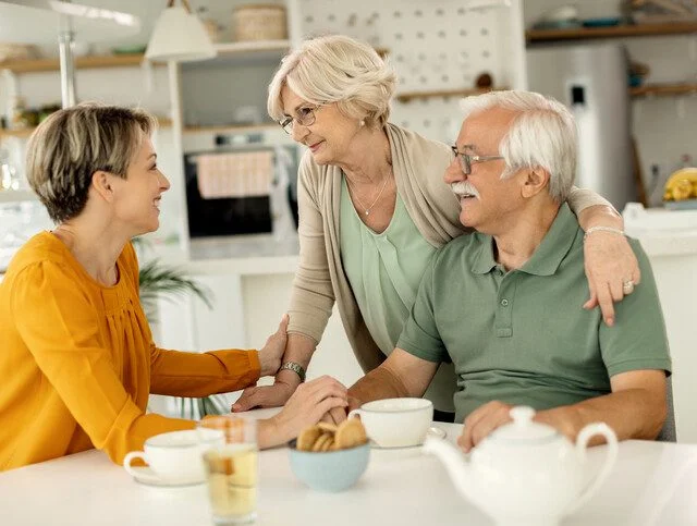 Older adult couple engages in conversation with adult daughter at table.