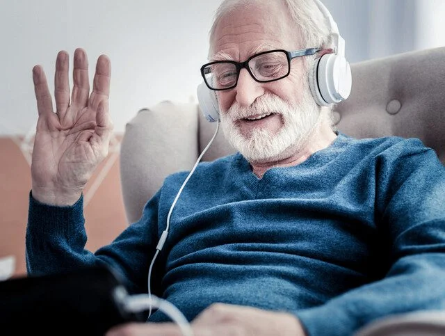 Positive nice joyful man smiling and waving his hand while greeting his family on a screen