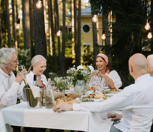 Smiling men and women around a table filled with wine, flowers, and delicious-looking food.