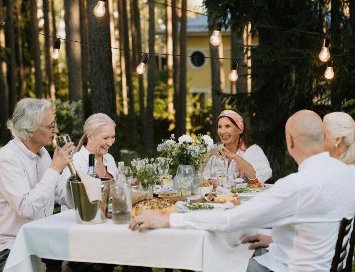 Smiling men and women around a table filled with wine, flowers, and delicious-looking food.