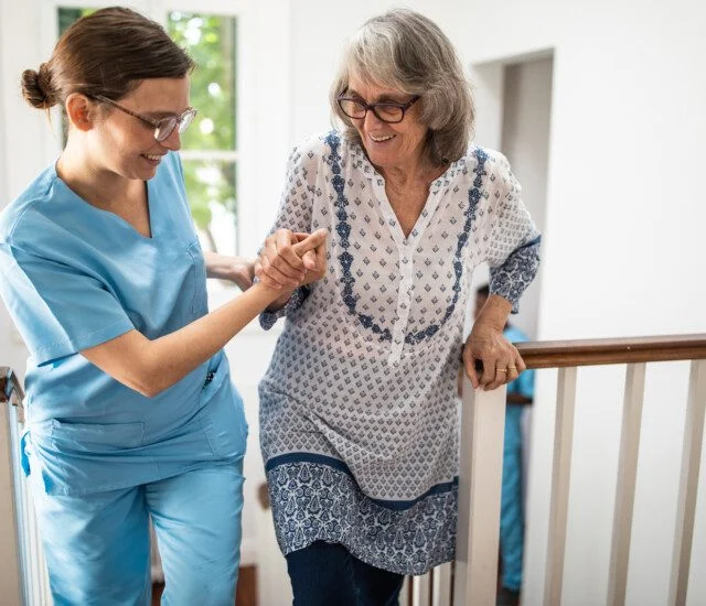 Female caregiver helping senior woman walking up stairs