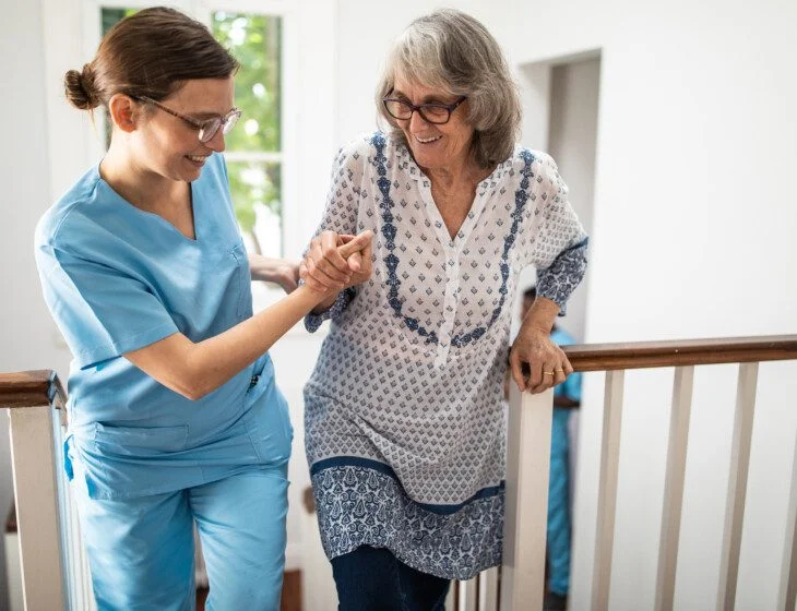 Female caregiver helping senior woman walking up stairs
