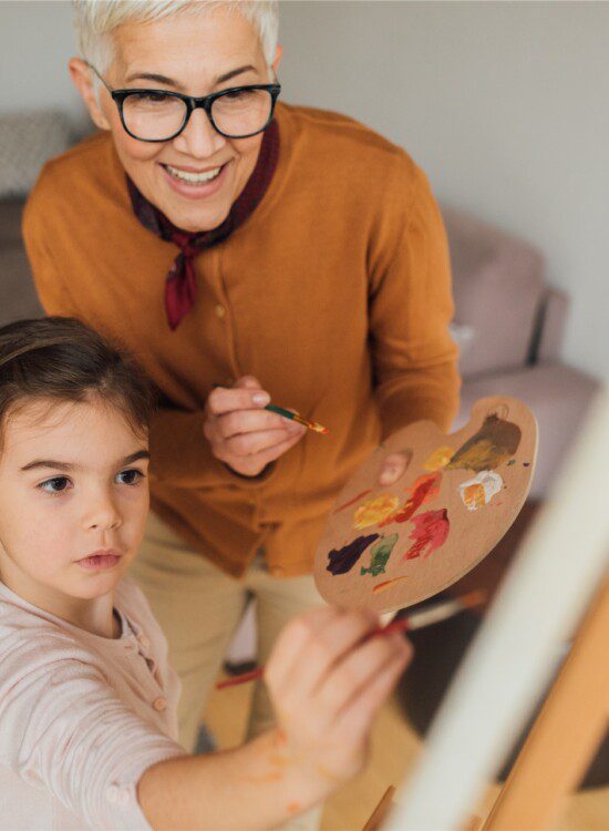 grandmother and girl with paintbrushes and canvas painting