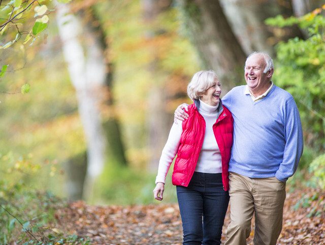 Two older adults walking in the woods on a brisk autumn day.