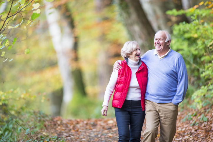 Two older adults walking in the woods on a brisk autumn day.