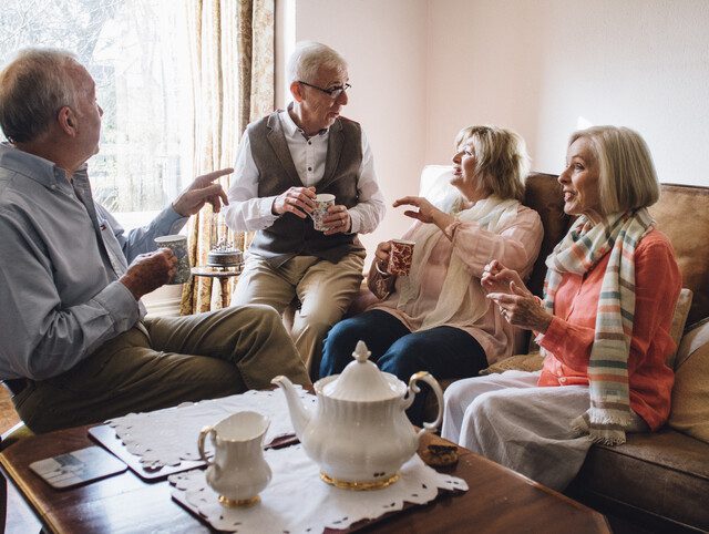 Older adults sitting around a table enjoying tea and conversation.