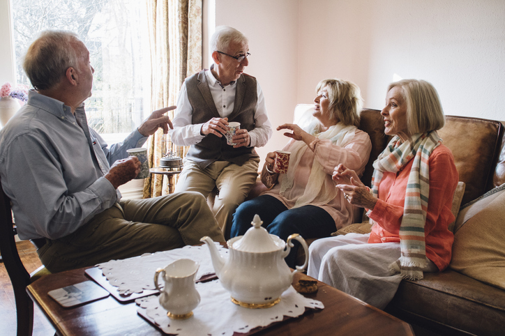 Older adults sitting around a table enjoying tea and conversation.